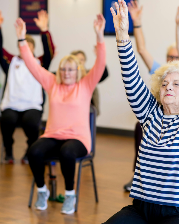 three older adults in chairs stretching their arms upwards