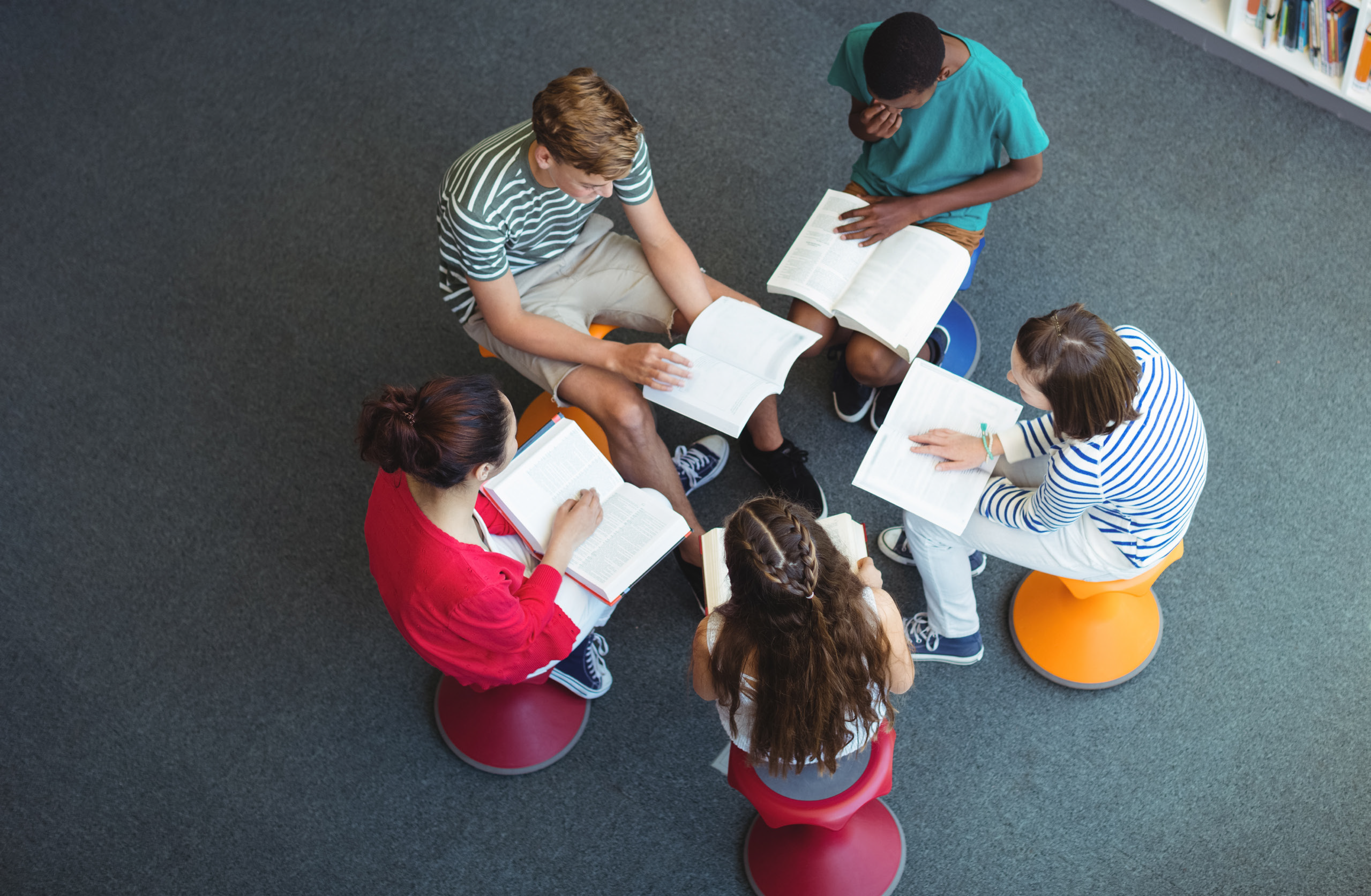 five young people sitting in a circle in a library reading together.