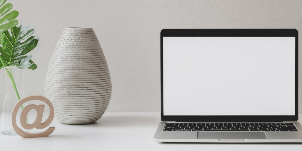 Laptop, vase, fern, and paperweight in the shape of an at sign